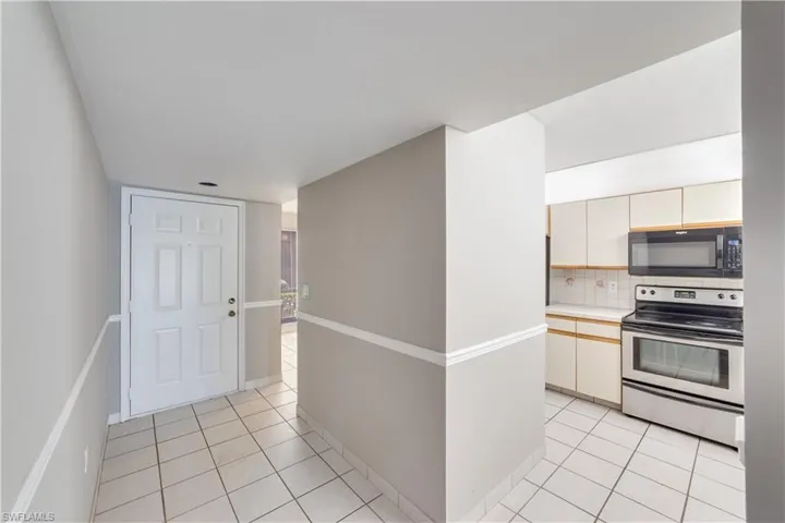 Kitchen with electric stove, backsplash, cream cabinets, and light tile floors