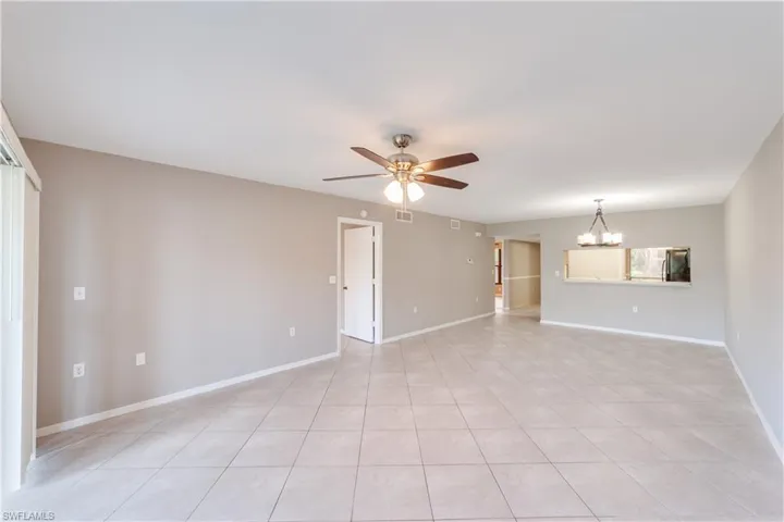 Tiled empty room with ceiling fan with notable chandelier