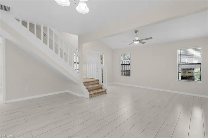 Unfurnished living room with light wood-style floors, stairway, lofted ceiling, and ceiling fan