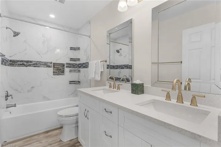 Full bath with shower / bathtub combination, double vanity, and wood finished floors