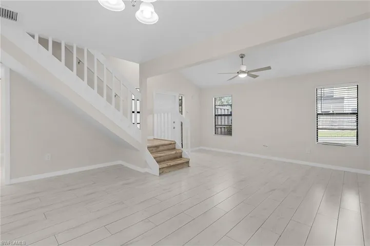 Unfurnished living room with light wood finished floors, stairs, vaulted ceiling, and a ceiling fan