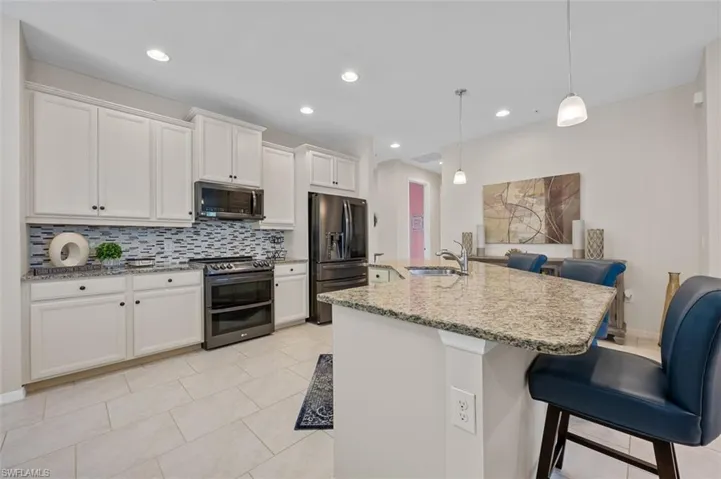 Kitchen with decorative backsplash, appliances with stainless steel finishes, white cabinetry, a sink, and a breakfast bar area