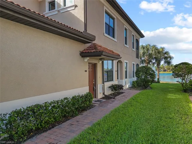 View of side of home featuring a tiled roof, a water view, stucco siding, and a lawn