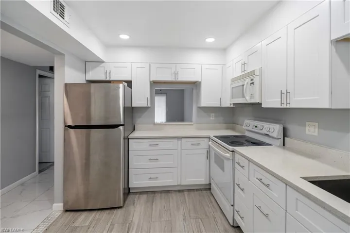 Kitchen featuring white appliances, white cabinetry, light stone counters, recessed lighting, and light wood-type flooring