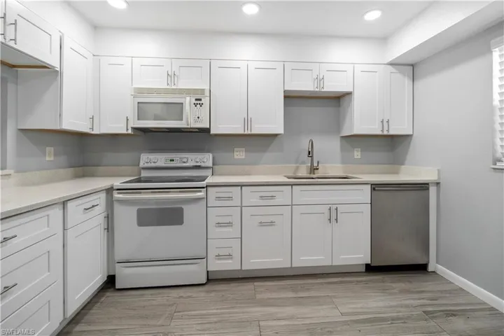 Kitchen featuring white appliances, white cabinetry, light stone counters, recessed lighting, and light wood-style flooring
