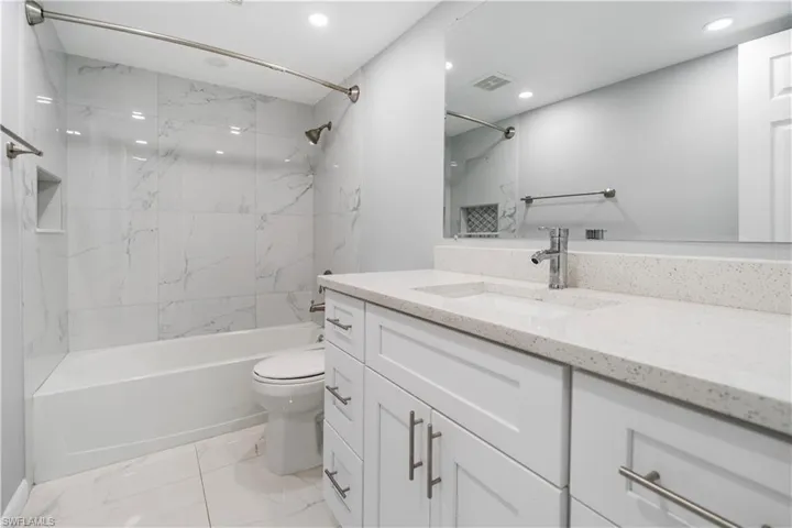 Bathroom featuring vanity, a combined bath / shower with marble appearance, light marble finish flooring, and recessed lighting