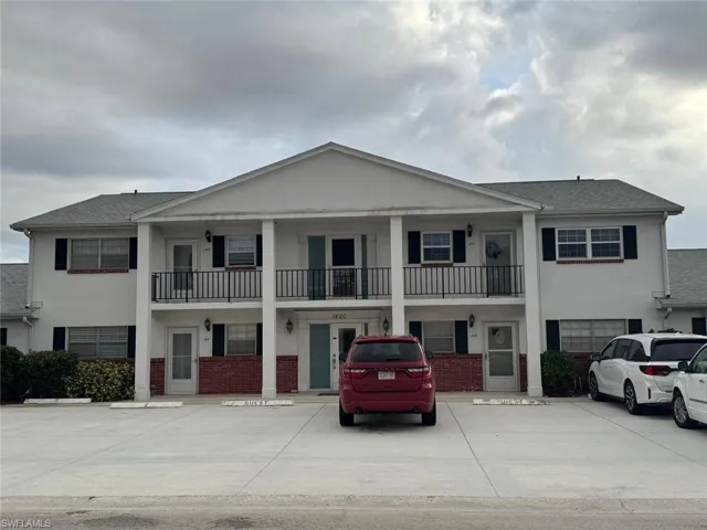 View of front of house with stucco siding, brick siding, uncovered parking, a balcony, and roof with shingles