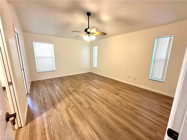 Empty room with wood finished floors, baseboards, a ceiling fan, and a wealth of natural light