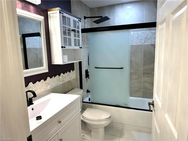 Bathroom with toilet, tile patterned floors, enclosed tub / shower combo, and vanity
