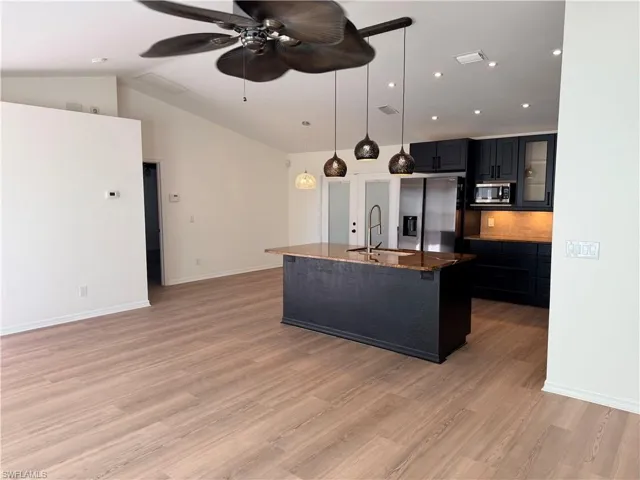 Kitchen with dark stone countertops, a kitchen island with sink, stainless steel appliances, hanging light fixtures, and a breakfast bar