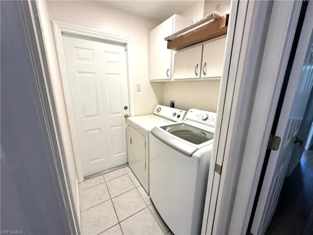 Clothes washing area with light tile patterned floors, separate washer and dryer, and cabinet space