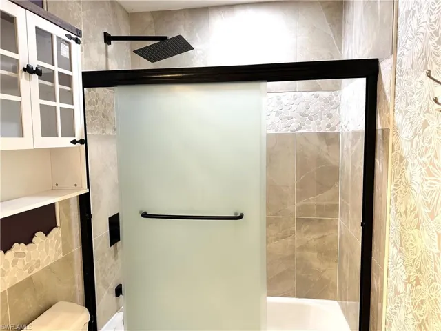 Full bathroom with toilet, tile walls, and a stall shower