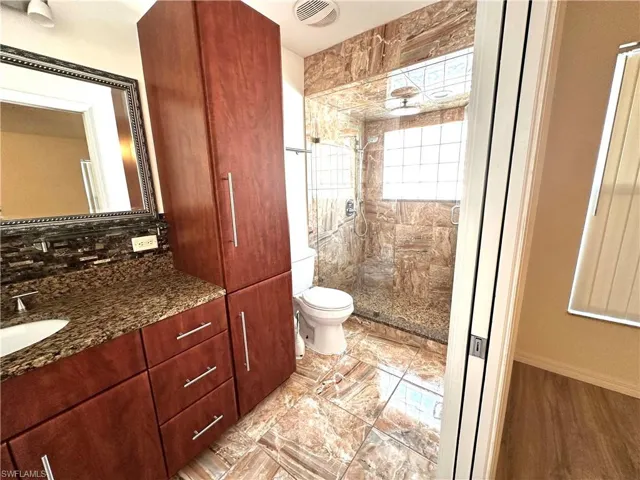 Bathroom with vanity, backsplash, toilet, a shower stall, and visible vents