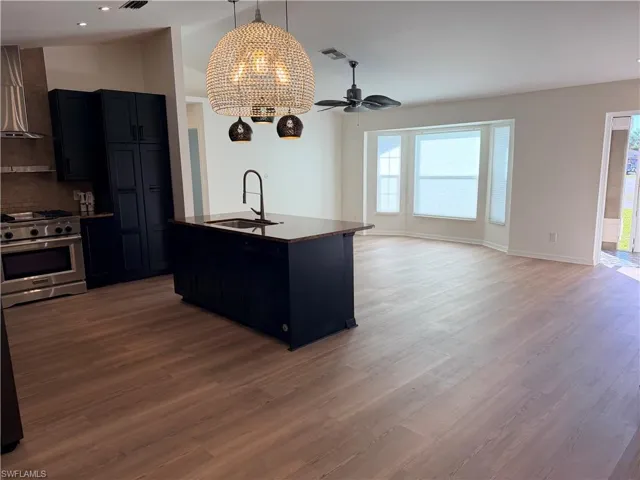 Kitchen featuring open floor plan, stainless steel gas stove, lofted ceiling, ceiling fan, and a kitchen island with sink
