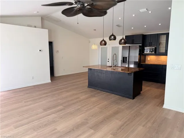 Kitchen with an island with sink, pendant lighting, dark stone counters, dark cabinets, and appliances with stainless steel finishes
