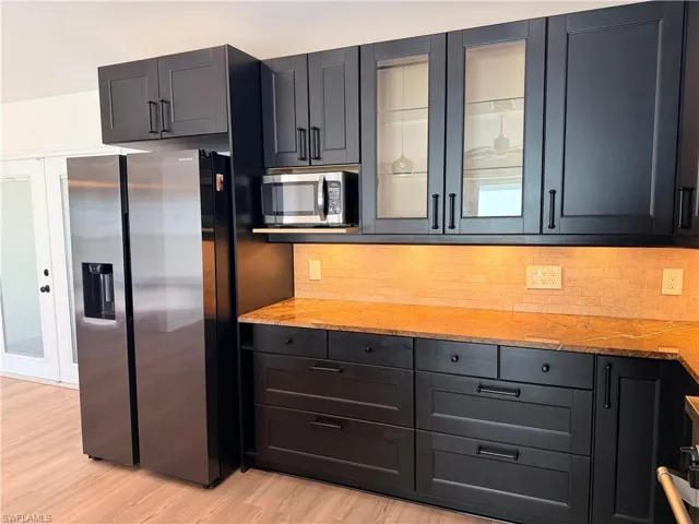 Kitchen with glass insert cabinets, appliances with stainless steel finishes, backsplash, light stone countertops, and light wood-style flooring