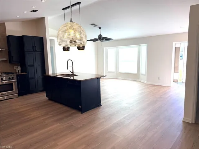 Kitchen featuring stainless steel range with gas cooktop, blue cabinetry, a ceiling fan, dark wood-style floors, and vaulted ceiling