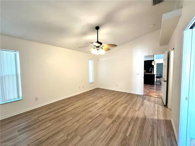 Spare room with baseboards, vaulted ceiling, a ceiling fan, visible vents, and wood finished floors