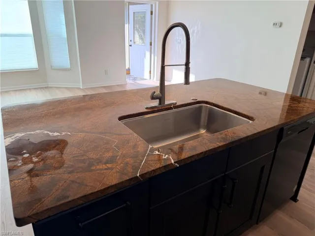 Kitchen featuring dark cabinetry, light wood-style flooring, and black dishwasher
