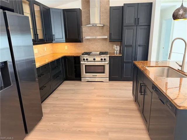 Kitchen with appliances with stainless steel finishes, wall chimney exhaust hood, decorative backsplash, light wood-type flooring, and light stone counters