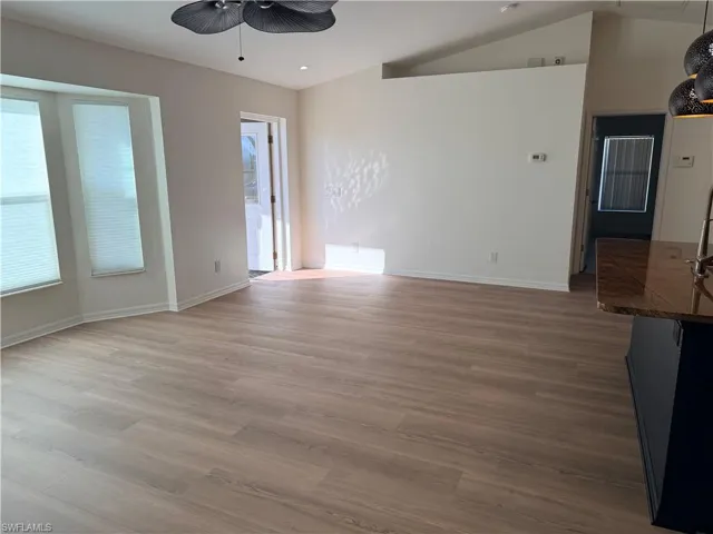 Empty room featuring light wood-style floors, a ceiling fan, and lofted ceiling