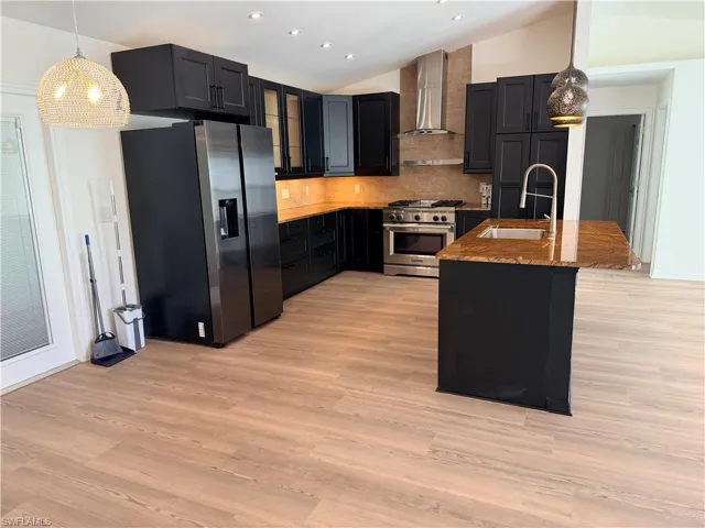 Kitchen with hanging light fixtures, vaulted ceiling, appliances with stainless steel finishes, glass insert cabinets, and an island with sink