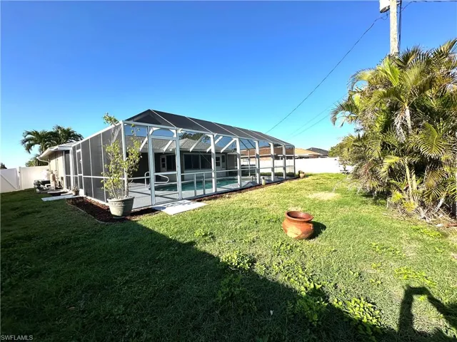 Back of house featuring a fenced backyard, glass enclosure, a fenced in pool, and a lawn