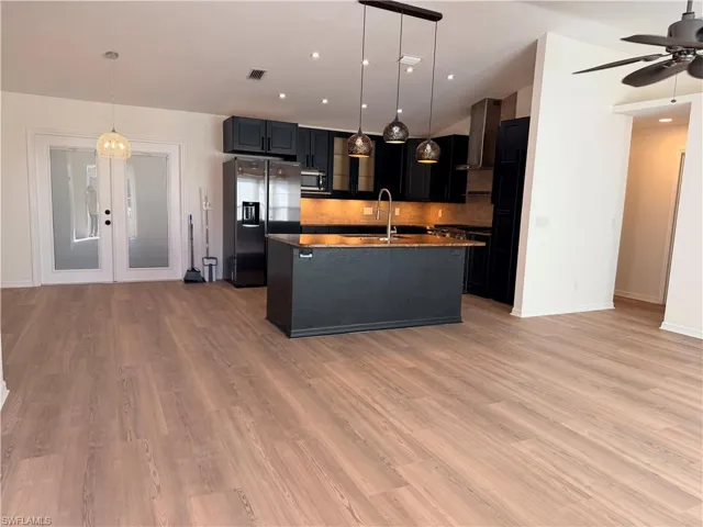 Kitchen featuring hanging light fixtures, dark cabinetry, stainless steel appliances, a center island with sink, and french doors