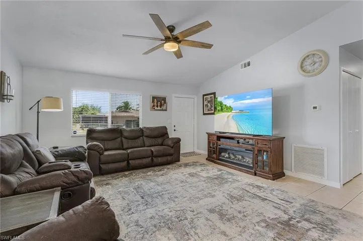 Living room featuring vaulted ceiling, ceiling fan, and light tile flooring
