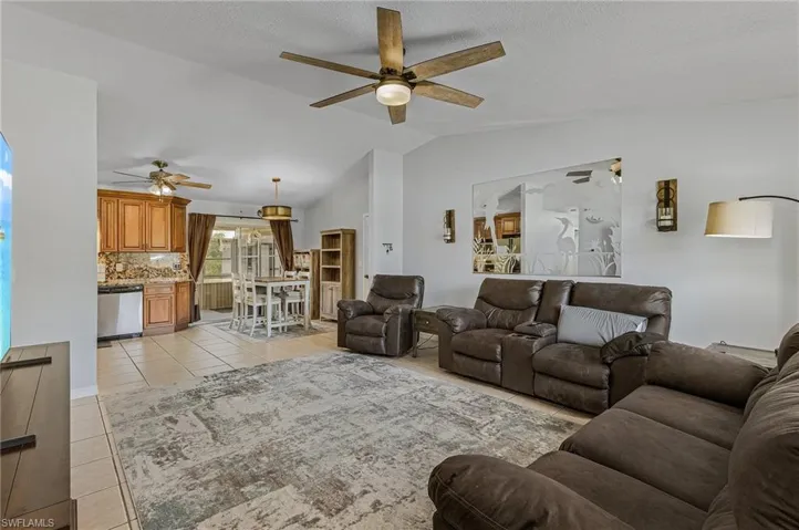 Living room featuring ceiling fan, light tile flooring, and lofted ceiling