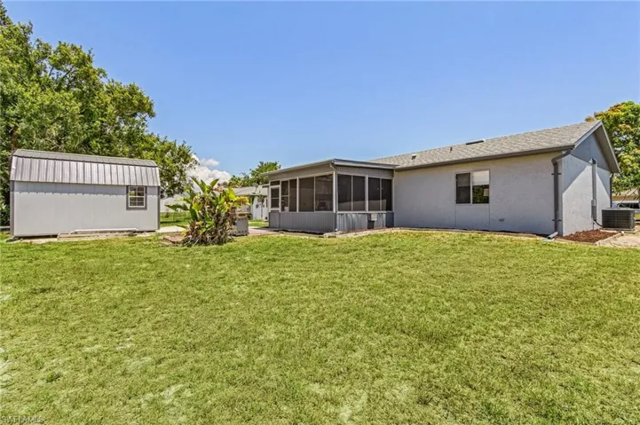 Rear view of house with a yard, a sunroom, an outdoor structure, and central air condition unit