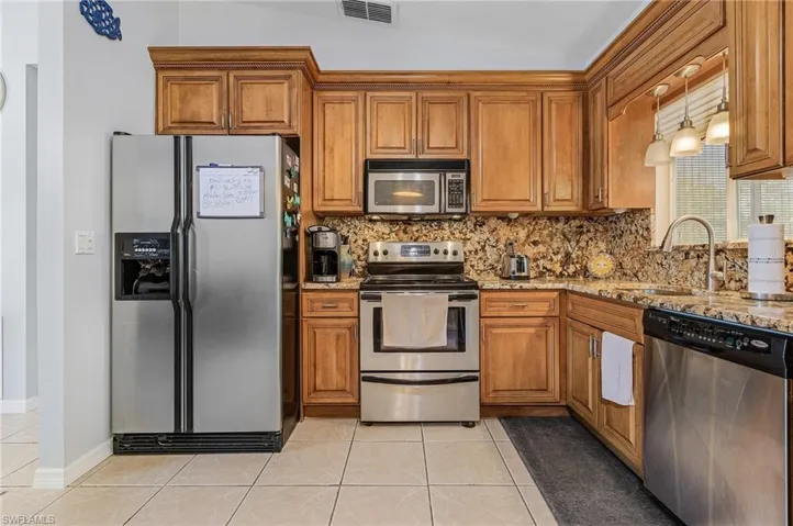 Kitchen with vaulted ceiling, light stone counters, appliances with stainless steel finishes, light tile floors, and pendant lighting