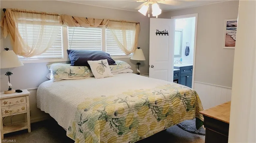 Bedroom featuring King size bed, carpet, a ceiling fan, ensuite bathroom, and wainscoting