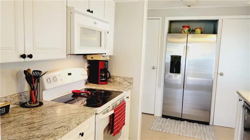 Kitchen with white cabinets, light tile patterned flooring, and light stone countertops.  Stackable washer/dryer cabinet on the right.