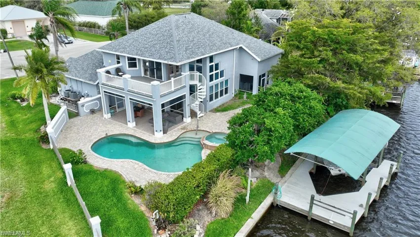 Rear view of property featuring a shingled roof, a patio, a pool with connected hot tub, a balcony, and stucco siding