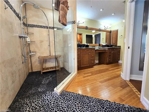 Full bath featuring double vanity, a stall shower, and light wood-type flooring
