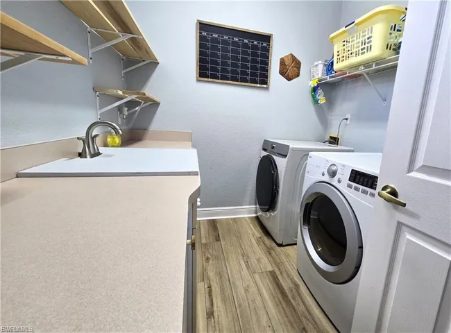 Laundry room featuring light wood-style floors, a textured wall, and washer and clothes dryer