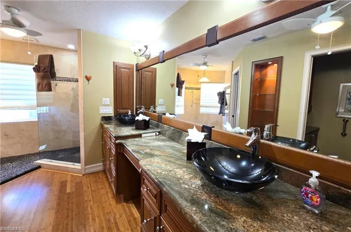 Bathroom featuring ceiling fan, walk in shower, vanity, light wood-type flooring, and a textured ceiling