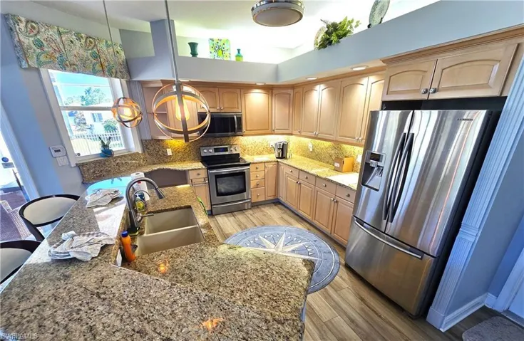 Kitchen with stainless steel appliances, light stone countertops, pendant lighting, light wood-type flooring, and a kitchen breakfast bar