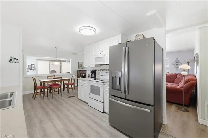 Kitchen with stainless steel appliances, white cabinetry, hanging light fixtures, light countertops, and light wood-style floors
