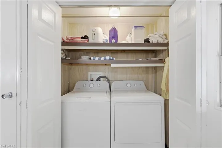 inside laundry area with washing machine and clothes dryer and wood walls
