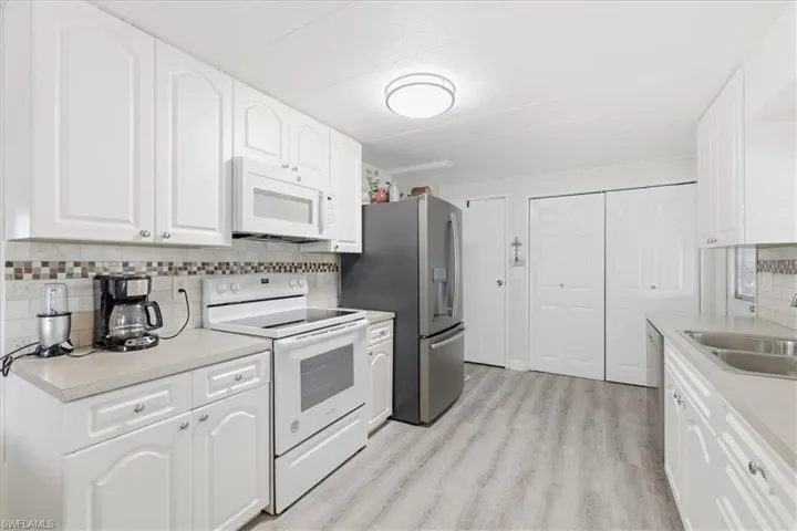 Kitchen featuring stainless steel appliances, light countertops, white cabinetry, and decorative backsplash