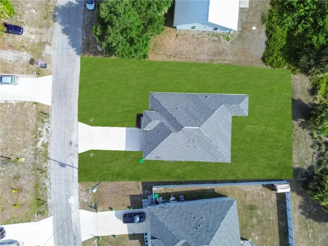 Property featuring a prominent shingle roof, expansive green lawn, and a light-colored driveway