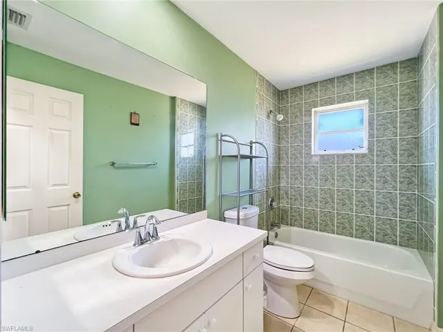 Full bathroom with tile flooring, tiled shower / bath combo, oversized vanity, and toilet