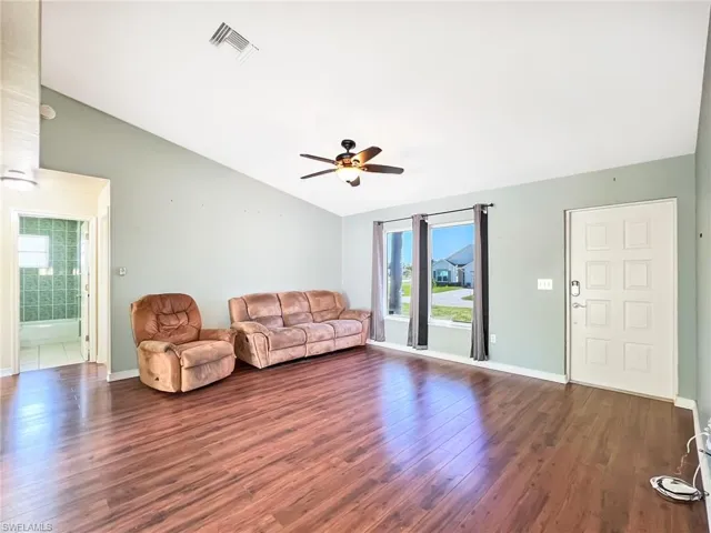 Living room featuring vaulted ceiling, ceiling fan, and dark tile floors