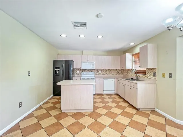 Kitchen with light brown cabinets, tasteful backsplash, sink, white appliances, and light tile floors