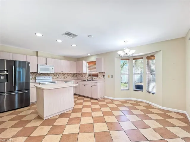 Kitchen with white appliances, backsplash, light tile flooring, and a kitchen island