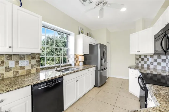Kitchen with ceiling fan, backsplash, sink, dark stone counters, and black appliances