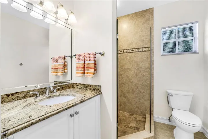 Bathroom with tiled shower, toilet, tile floors, and single sink
