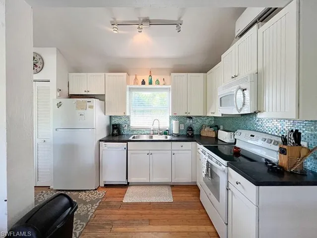 Kitchen with white appliances, sink, backsplash, light hardwood / wood-style floors, and rail lighting